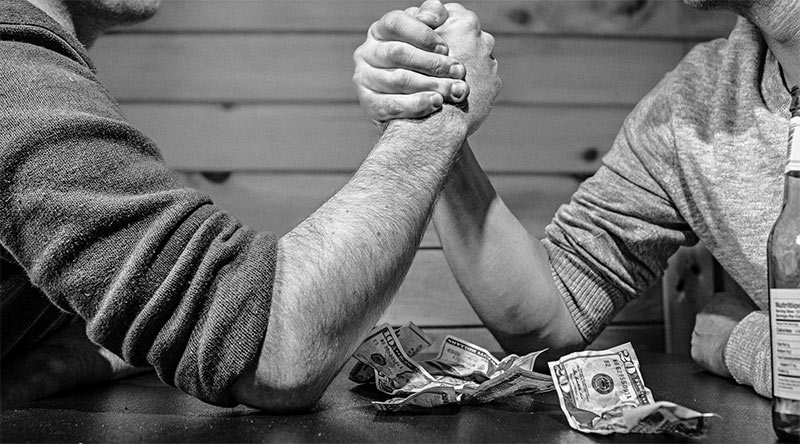 two men arm wrestling with money and alcohol on the table